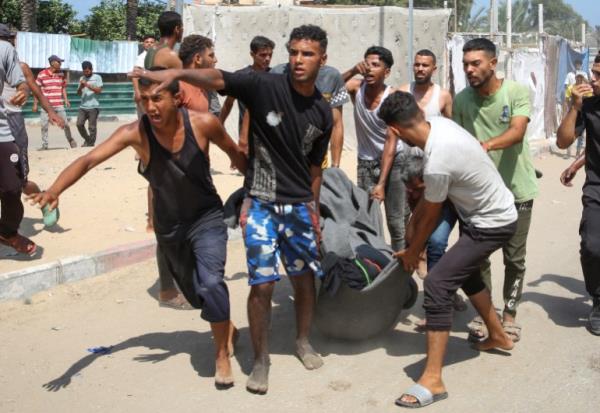 People carry a casualty at the site of what Palestinians say was an Israeli strike at a tent camp in Al-Mawasi area