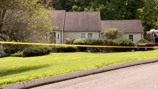 A suburban house with police tape around the lawn.