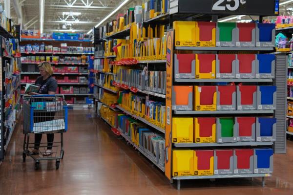 People shopping for school supplies inside a Walmart in Edmond, Okla., with a focus on a woman looking at items on a shelf.