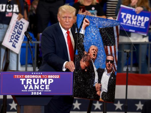 Republican presidential nominee, former U.S. President Do<em></em>nald Trump holds an artwork that he signed for the artist of Trump during the assassination attempt, during a campaign rally at the Georgia State University Co<em></em>nvocation Center on August 03, 2024, in Atlanta, Georgia. 