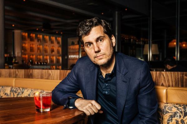 Scott Sartiano sitting at a table with a drink in his restaurant, Sartiano's, in Soho, Manhattan