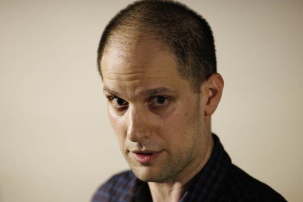 Evan Gershkovich, a Wall Street Journal reporter with short hair and wearing a plaid shirt, seen at Andrews Air Force ba<em></em>se during a priso<em></em>ner swap, with President Joe Biden present.