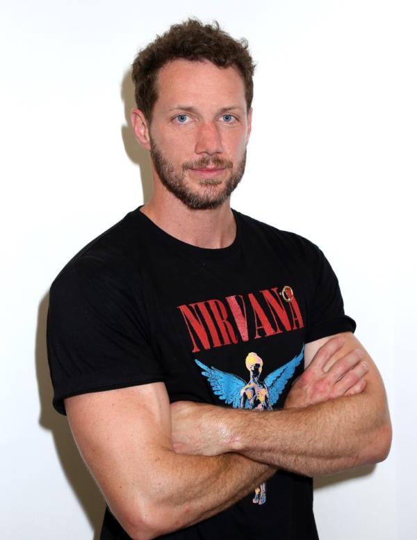 Johnny Wactor wearing a black Nirvana shirt with his arms folded.