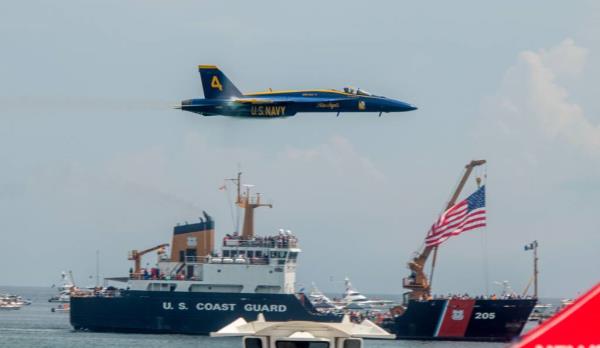 A U.S. Navy Blue Angels jet plane flies over a US Coast Guard ship at an air show over Pensacola Beach