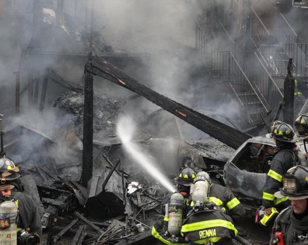 FDNY firefighters spraying water at the fire on the remains of a house.