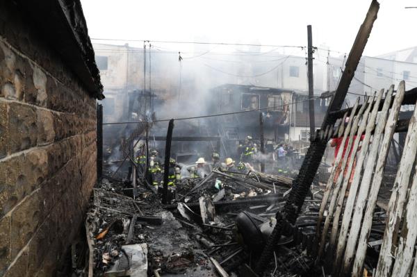 Firefighters working at the debris-filled backyard of a house destroyed by a 5-alarm fire in Queens, NY.