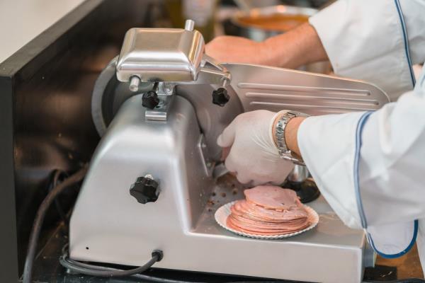 Chef in rubber gloves using a ham slicer machine in supermarket deli