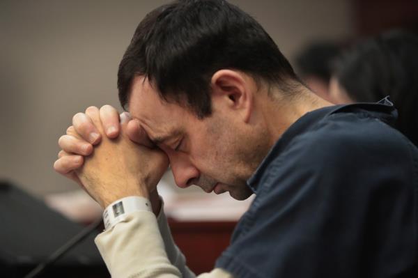 Larry Nassar, disgraced USA Gymnastics doctor, seated with eyes closed and hands folded, showing physical scars from prison attack