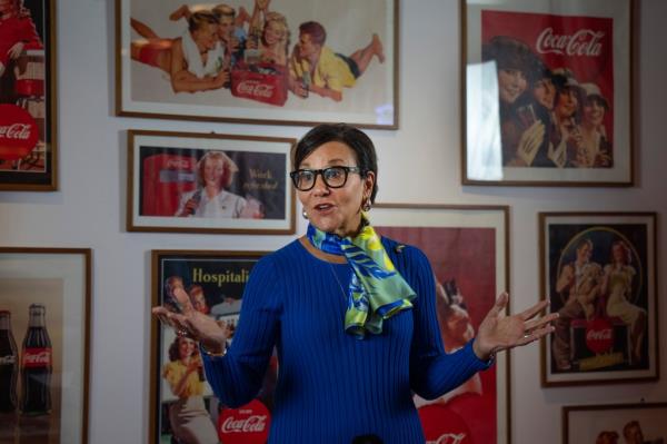 Penny Pritzker in front of Coca-Cola f<em></em>ramed posters