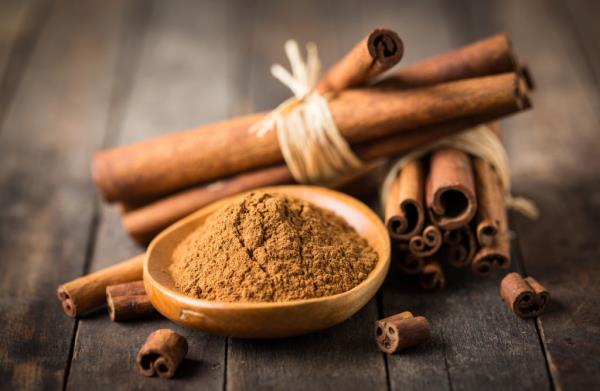 A bowl of powdered cinnamon next to whole cinnamon sticks.