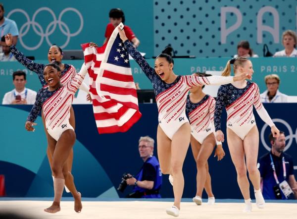 Team USA gymnasts including Simone Biles and Suni hold the American flag.