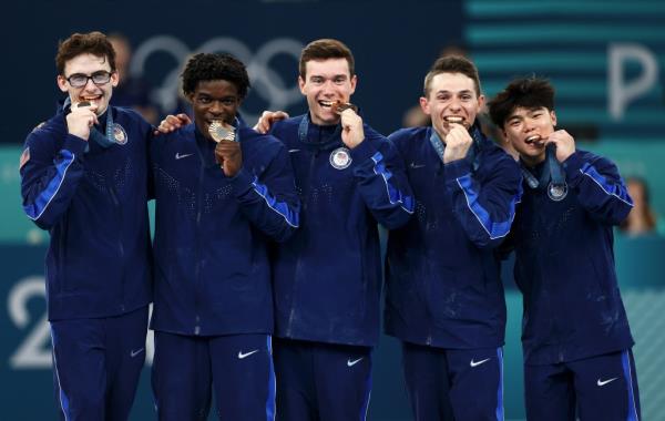 Bro<em></em>nze medalists Paul Juda, Frederick Richard, Stephen Nedoroscik, Brody Malone and Asher Hong bite into their bro<em></em>nze medals.