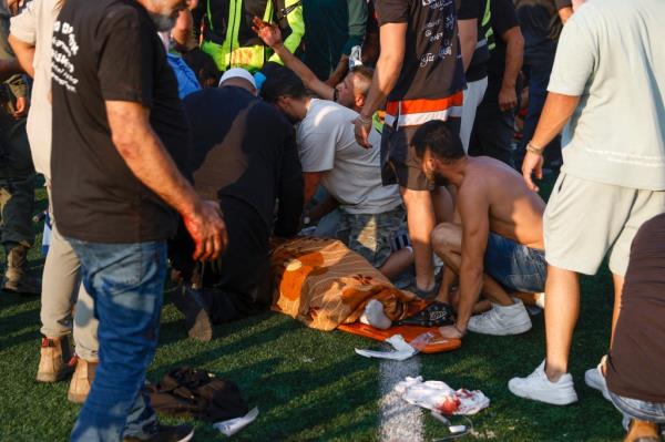 Israelis surround a dead body covered in a blanket on a soccer field.