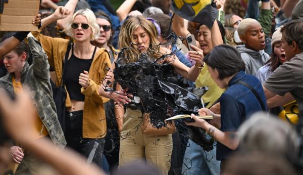 Jennifer Aniston with her eyes closed and oil getting thrown on her. 