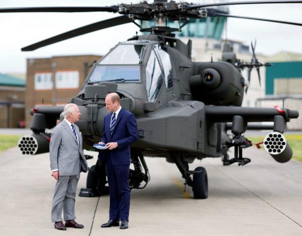 King Charles III and Prince William, wearing the regimental tie of the Army Air Corps, standing in front of an Apache helicopter during the official handover ceremony at the Army Aviation Centre, Stockbridge, England